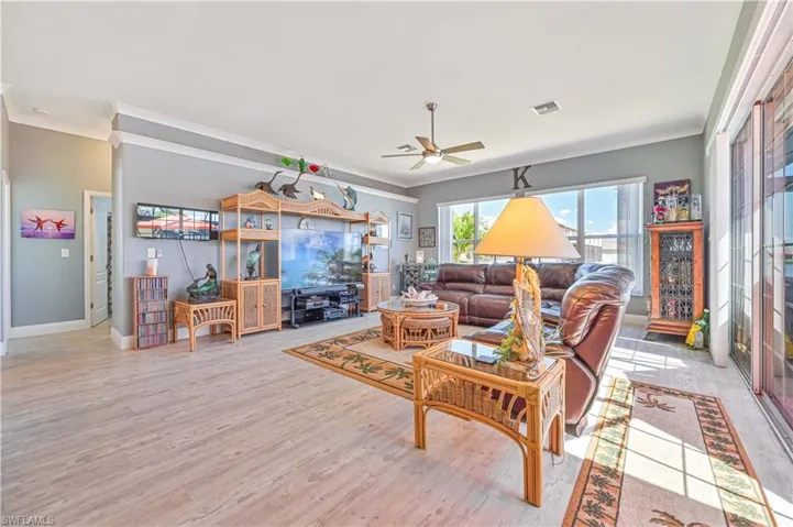 Living area with a ceiling fan, visible vents, ornamental molding, and light wood-style floors