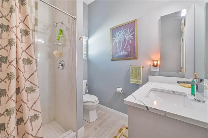 Full bath with vanity, wood finished floors, toilet, baseboards, and a shower with shower curtain