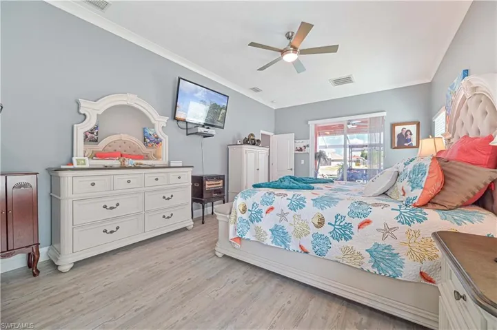 Bedroom with ceiling fan, visible vents, ornamental molding, and light wood-style floors