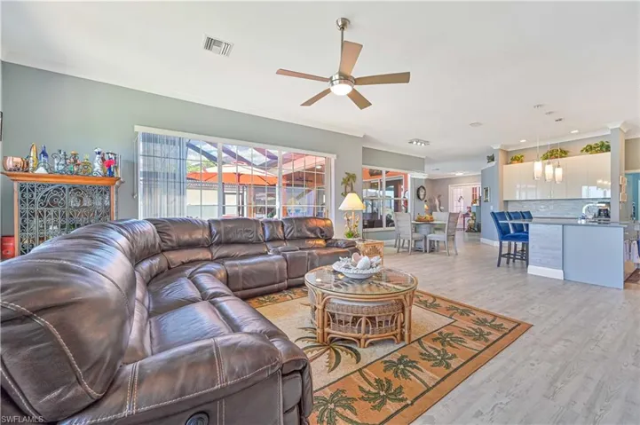 Living area with light wood-style floors, ornamental molding, a ceiling fan, and visible vents