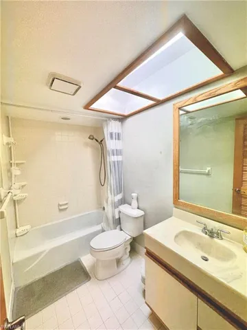 Bathroom featuring a skylight, white tiled flooring, a built-in vanity with integrated sink, and a bathtub with tiled surround