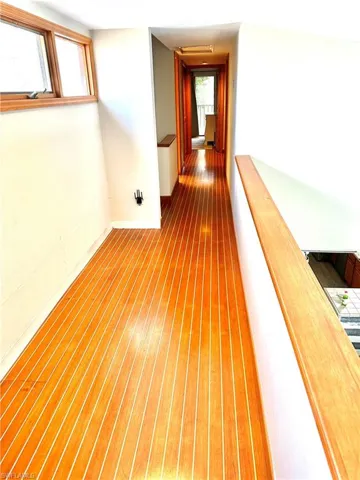 Second-level hallway featuring strip wood flooring, natural wood window trim, natural wood railings, and recessed ceiling lighting