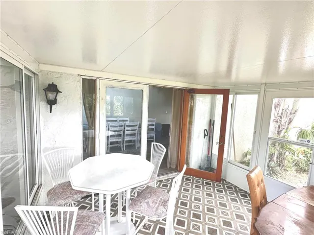 Enclosed patio featuring patterned floor tiling, an exterior wall sconce, and multiple windows