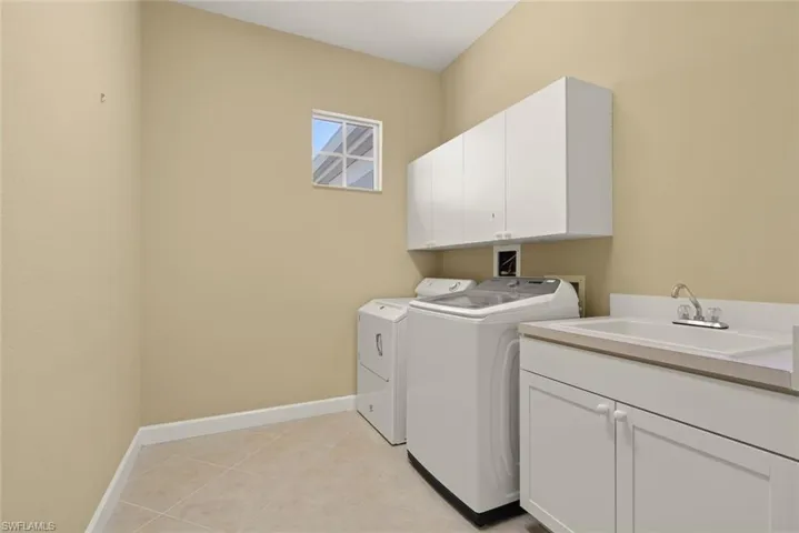 Laundry area with baseboards, light tile patterned flooring, separate washer and dryer, cabinet space, and a laundry tub