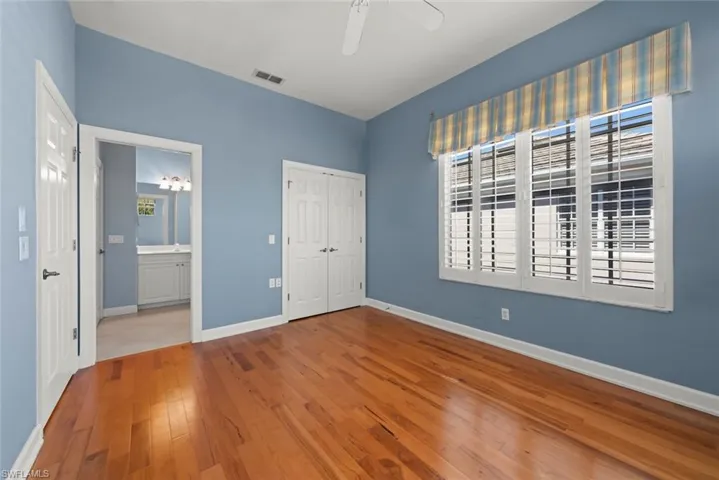 Bedroom featuring wood flooring, ceiling fan, closet, plantation shutters and electric hurricane exterior shutters.
