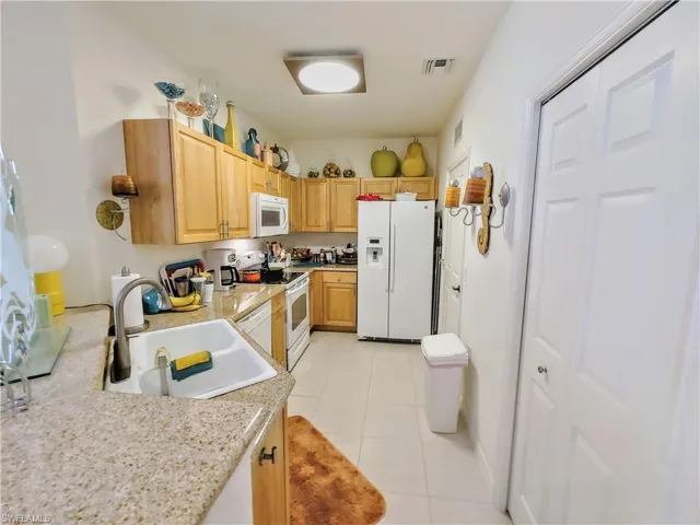 Kitchen featuring white appliances, sink, light tile patterned floors, light brown cabinetry, and light stone counters
