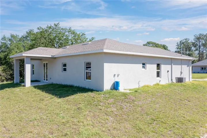 Back of property with central AC unit, stucco siding, and a yard