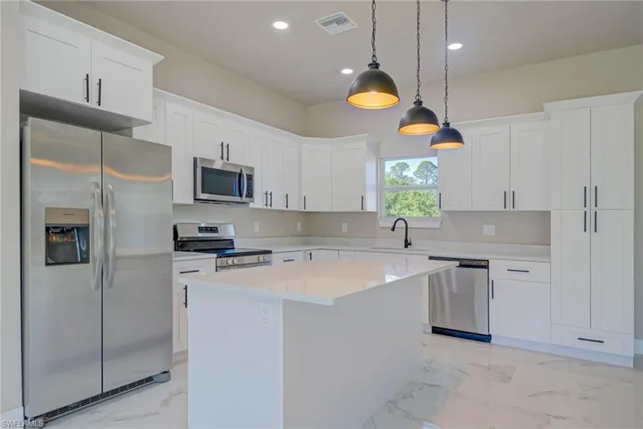 Kitchen with stainless steel appliances, marble finish floor, a kitchen island, a sink, and visible vents