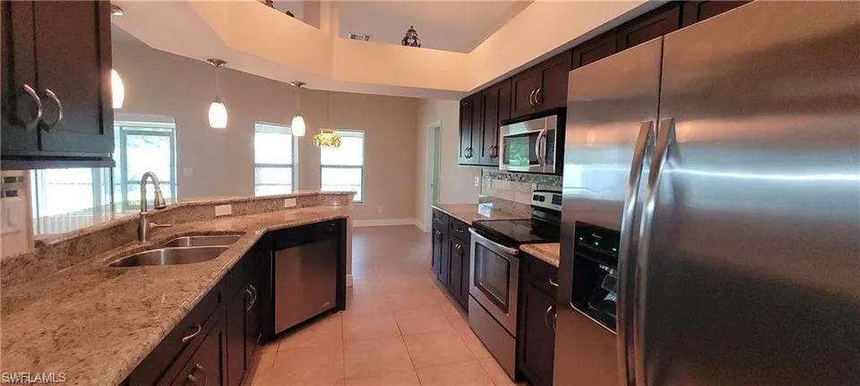 Kitchen with light stone counters, hanging light fixtures, light tile patterned floors, sink, and appliances with stainless steel finishes