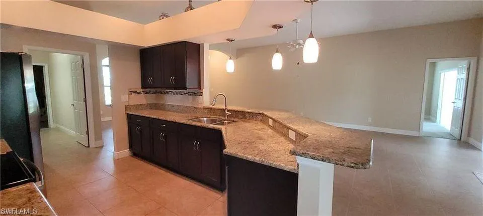 Kitchen featuring light stone counters, stainless steel fridge, sink, kitchen peninsula, and pendant lighting
