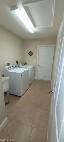 Clothes washing area featuring washing machine and dryer, sink, and light tile patterned floors