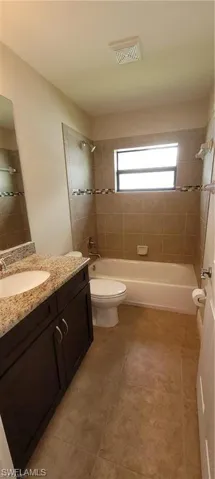 Full bathroom with vanity, tiled shower / bath combo, toilet, and tile patterned floors