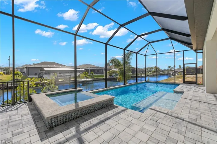 View of swimming pool with a lanai, an in ground hot tub, a water view, and a patio