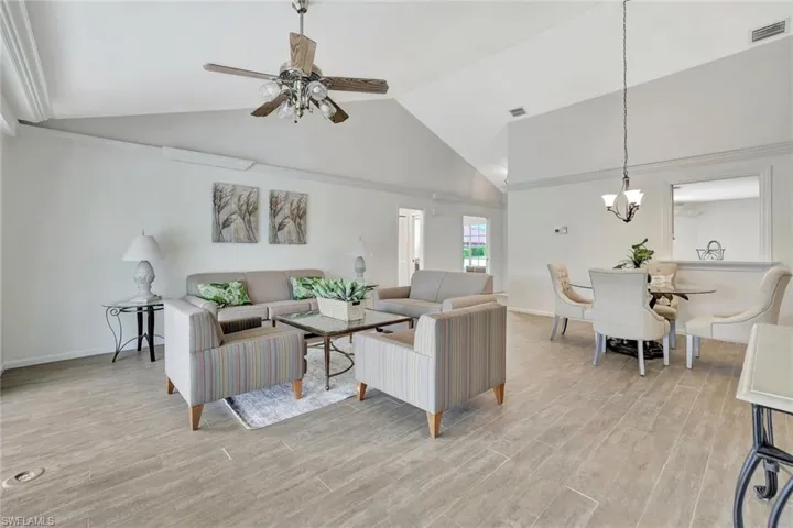 Living room with a chandelier, high vaulted ceiling, ceiling fan, light wood-style flooring, and baseboards