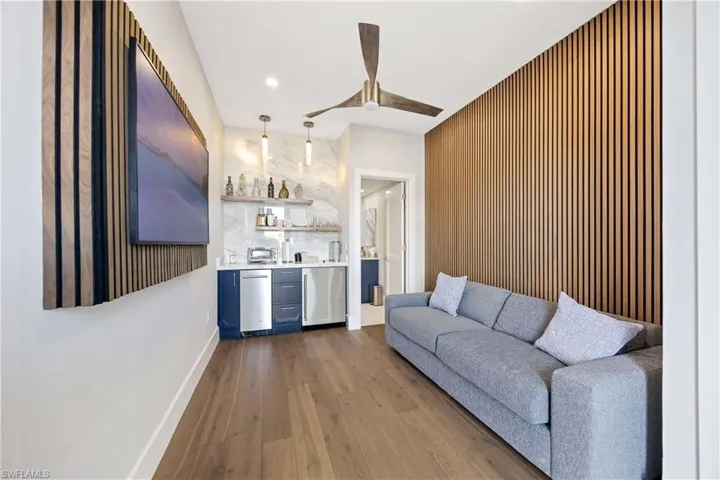 Living room with dark wood-style floors, wet bar, ceiling fan, an accent wall, and recessed lighting