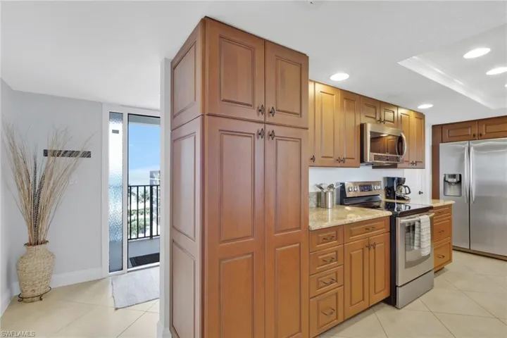 Kitchen featuring appliances with stainless steel finishes, light stone countertops, brown cabinets, recessed lighting, and light tile patterned flooring
