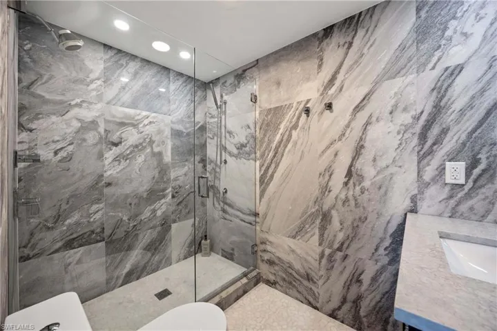 Full bath featuring vanity, recessed lighting, a marble finish shower, and tile walls