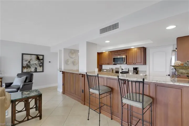 Kitchen with brown cabinets, light stone counters, a breakfast bar area, recessed lighting, and stainless steel appliances