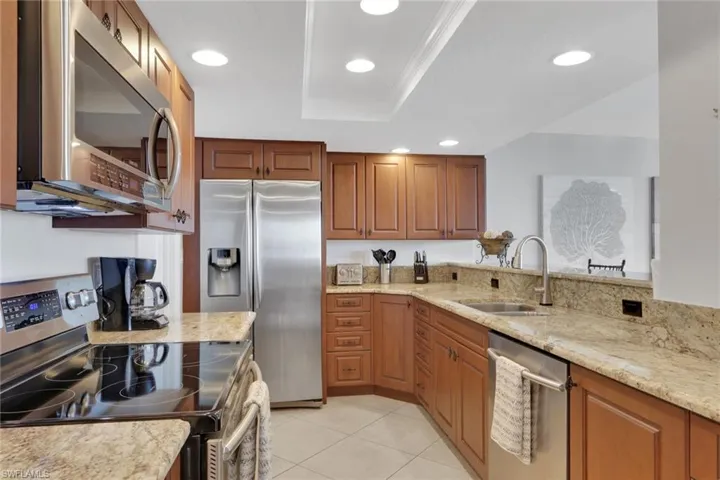 Kitchen with stainless steel appliances, brown cabinets, light stone countertops, recessed lighting, and light tile patterned floors