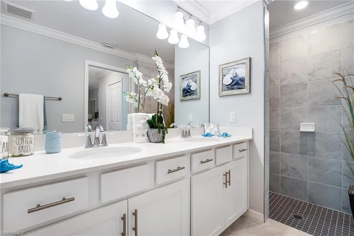 Bathroom featuring double vanity, ornamental molding, and walk in shower