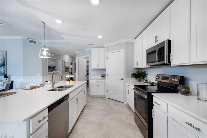 Kitchen featuring stainless steel appliances, ornamental molding, hanging light fixtures, white cabinetry, and a kitchen island with sink