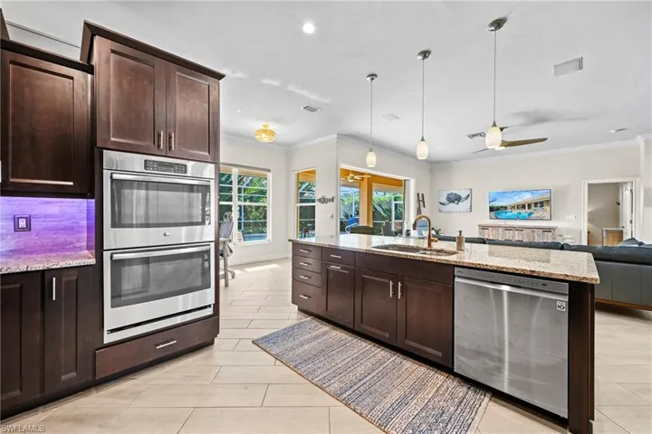 Kitchen with light stone counters, dark wood finish cabinets, stainless steel appliances, open floor plan, and ornamental molding