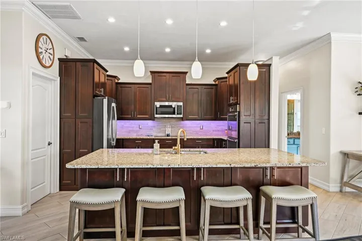 Kitchen featuring a kitchen breakfast bar, light stone counters, hanging light fixtures, a spacious island, and wood finish floors