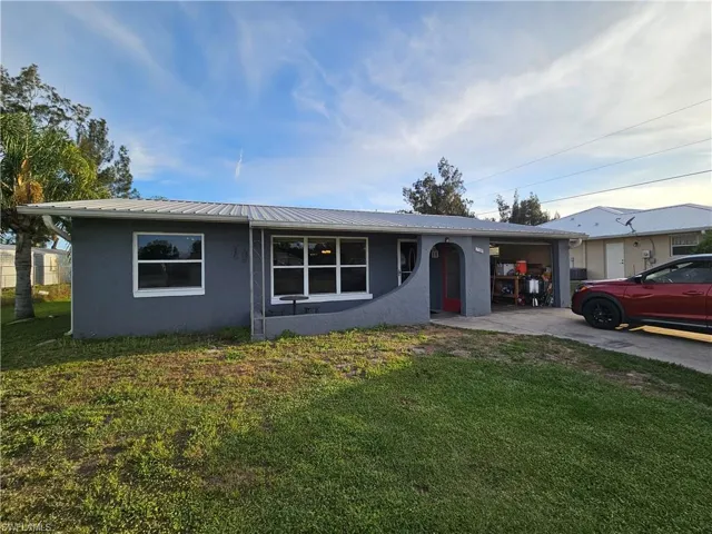 Single story home featuring metal roof, an attached garage, concrete driveway, a front yard, and stucco siding