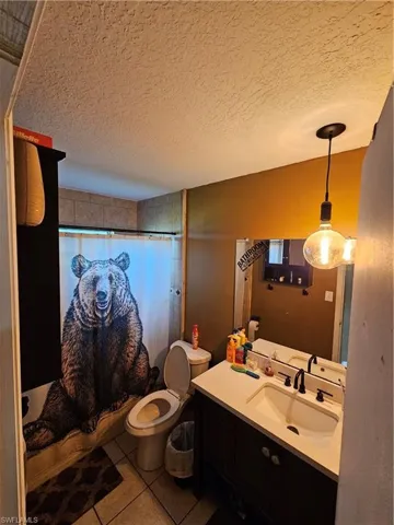 Bathroom with a textured ceiling, toilet, tile patterned floors, vanity, and a shower with curtain