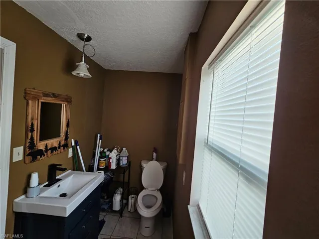 Bathroom featuring a textured ceiling, toilet, tile patterned floors, and vanity