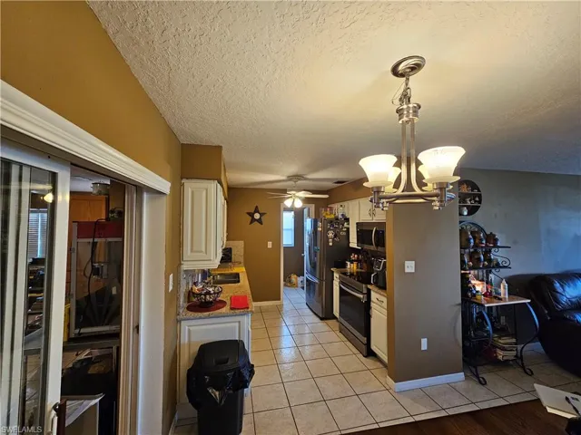 Kitchen featuring appliances with stainless steel finishes, a textured ceiling, light tile patterned floors, ceiling fan with notable chandelier, and decorative light fixtures