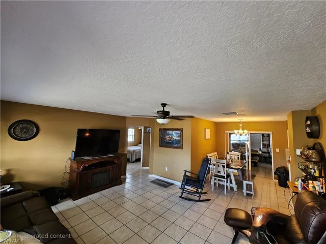 Living area with light tile patterned flooring, a textured ceiling, visible vents, baseboards, and ceiling fan with notable chandelier