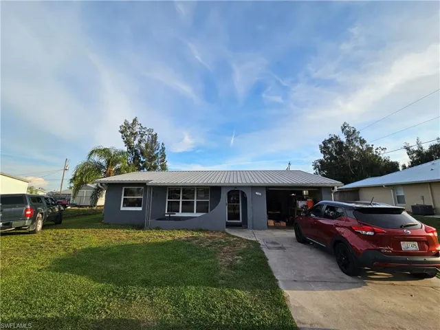 Single story home featuring driveway, a front yard, stucco siding, metal roof, and a garage