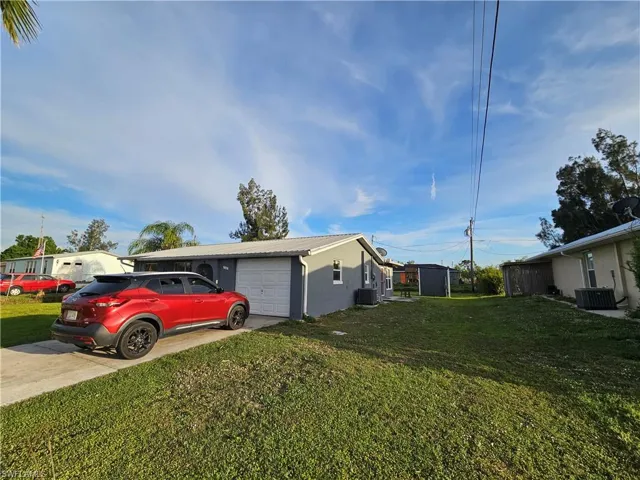 View of side of property featuring a garage, driveway, central air condition unit, and metal roof