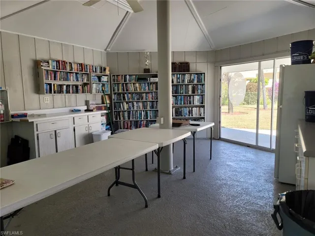 Home office featuring vaulted ceiling, wooden walls, and wall of books