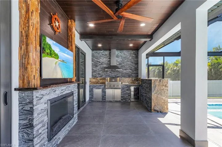 View of patio with beverage cooler, fence, glass enclosure, exterior kitchen, and a fenced in pool