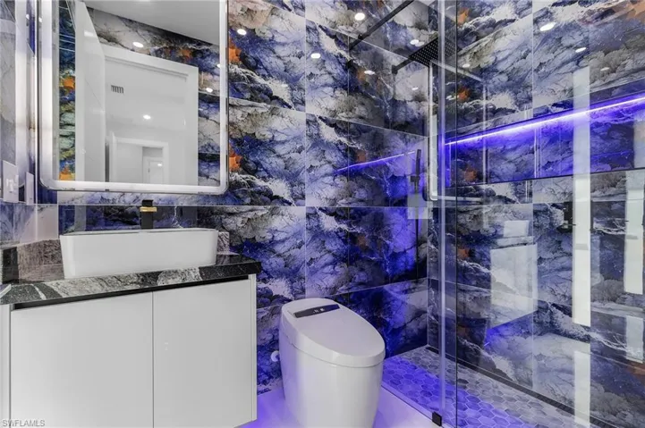 Bathroom featuring vanity, tile walls, toilet, and a tile shower