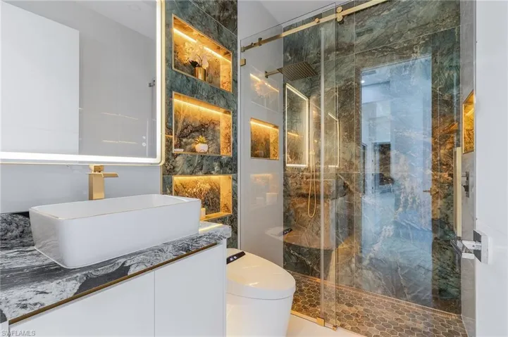 Bathroom with vanity, toilet, and a marble finish shower