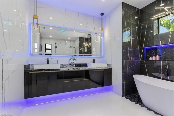 Full bath with a sink, a freestanding bath, tile walls, and double vanity