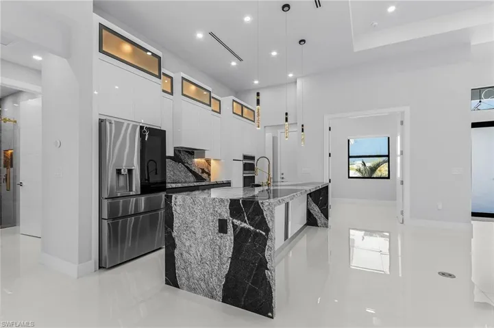Kitchen featuring a spacious island, light stone countertops, white cabinets, stainless steel appliances, and modern cabinets