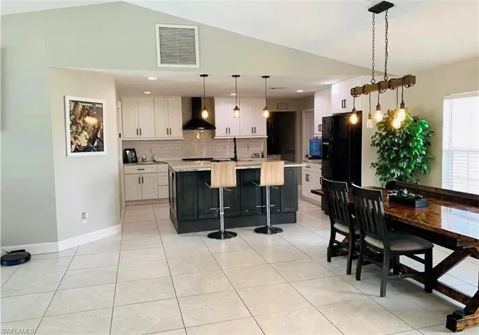 Kitchen with a center island with sink, decorative backsplash, pendant lighting, white cabinetry, and black fridge with ice dispenser