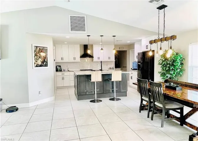 Kitchen featuring a center island with sink, white cabinets, a kitchen bar, tasteful backsplash, and vaulted ceiling
