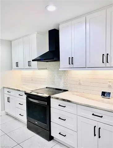Kitchen featuring black range with electric cooktop, white cabinetry, decorative backsplash, and wall chimney exhaust hood