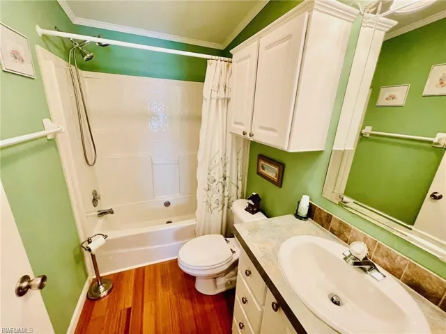 Full bath with ornamental molding, shower / bath combination with curtain, vanity, and wood finished floors