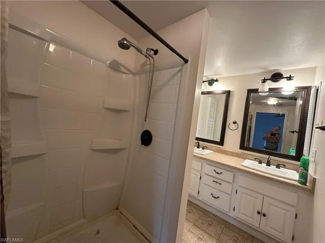 Bathroom with tiled shower, double sink vanity, and tile patterned flooring
