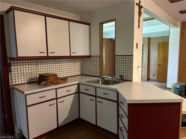 Kitchen located Downstairs with kitchen peninsula, white cabinets, tile walls, decorative backsplash, and sink