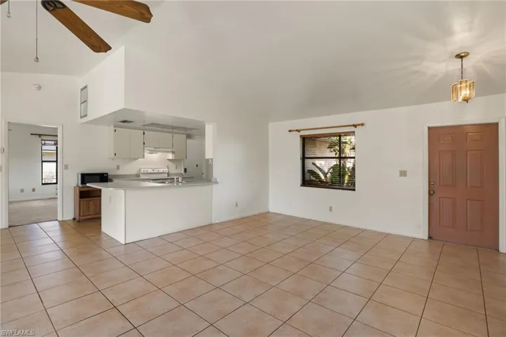 Unfurnished living room featuring light tile patterned flooring, ceiling fan with notable chandelier, a wealth of natural light, and high vaulted ceiling