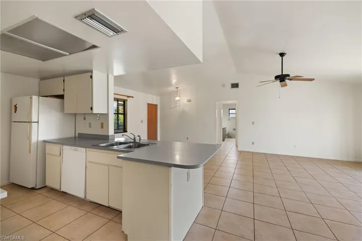Kitchen featuring sink, white appliances, vaulted ceiling, and light tile patterned floors
