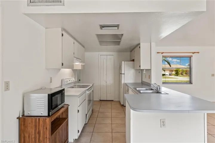 Kitchen with electric stove, sink, white cabinetry, and kitchen peninsula