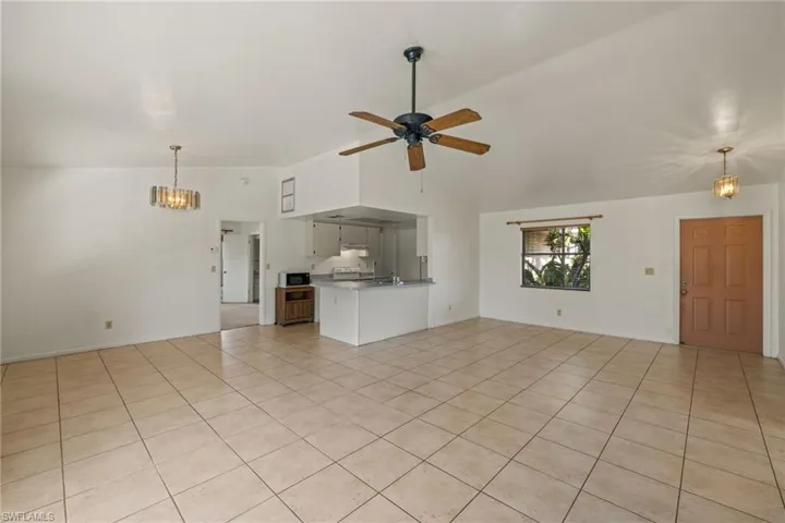 Unfurnished living room with vaulted ceiling, ceiling fan with notable chandelier, and light tile patterned floors